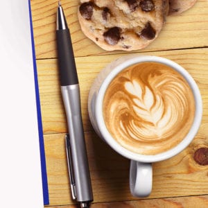 Pen on wooden background with coffee and chocolate chip cookies.